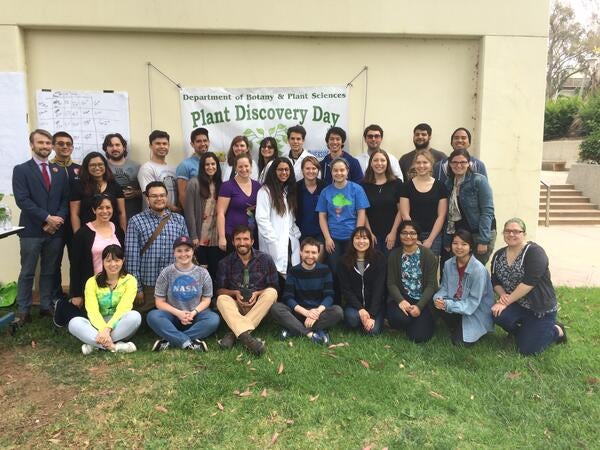 Group photograph of the volunteers for Plant Discovery Day- 3 rows of people standing in front of a Plant Discovery Day banner