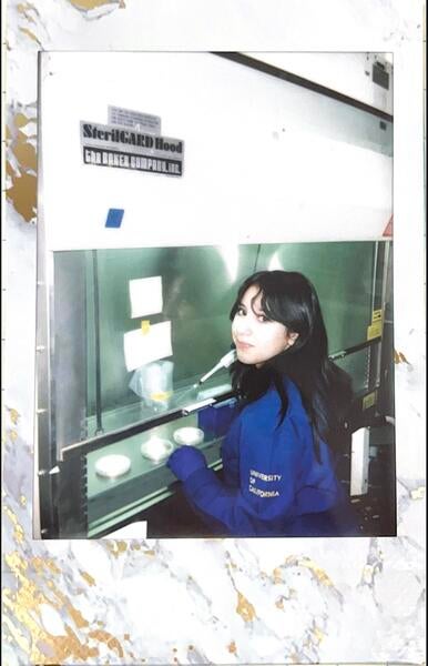 Person sitting in front of a fume hood in a blue lab coat holding a pipette