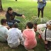 Male graduate student squatting in front of three 5th grade students who are sitting on the ground in front of potted plants